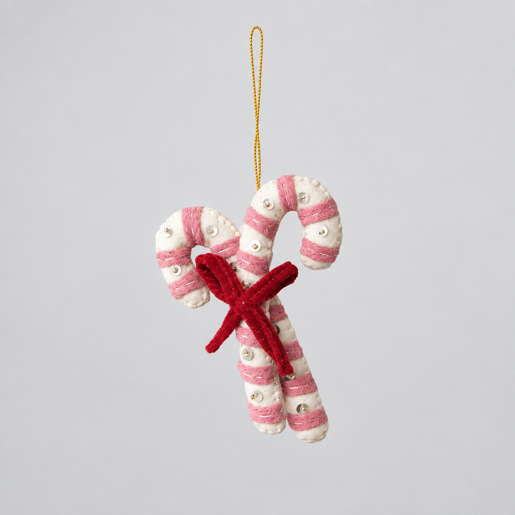 A felted wool candy cane ornament with pink and white stripes, small silver bead accents, and a red felted bow, hanging from a gold string on a white background.