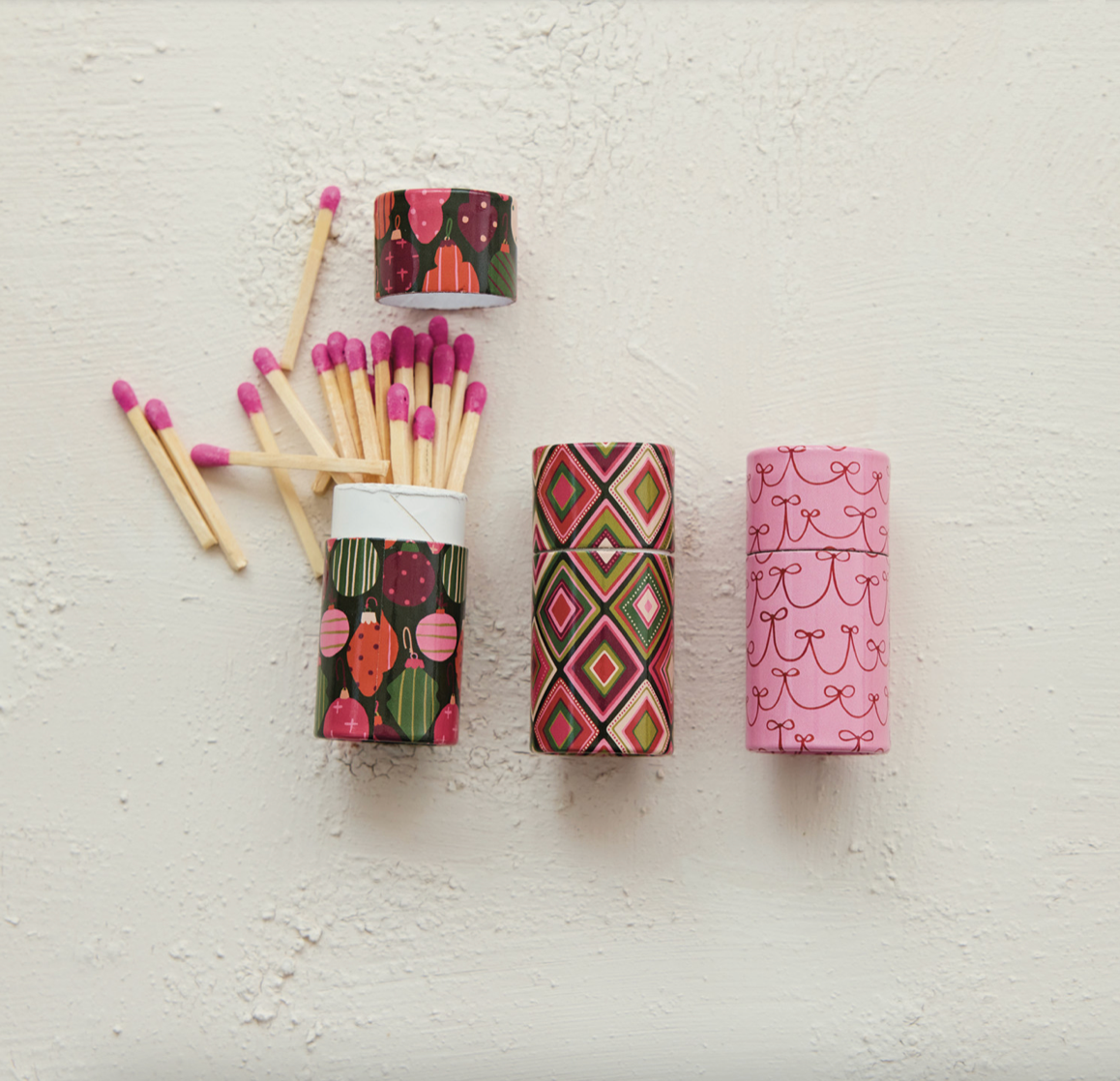 Three decorative matchboxes with colorful patterns and pink-tipped matches arranged on a textured off-white background.