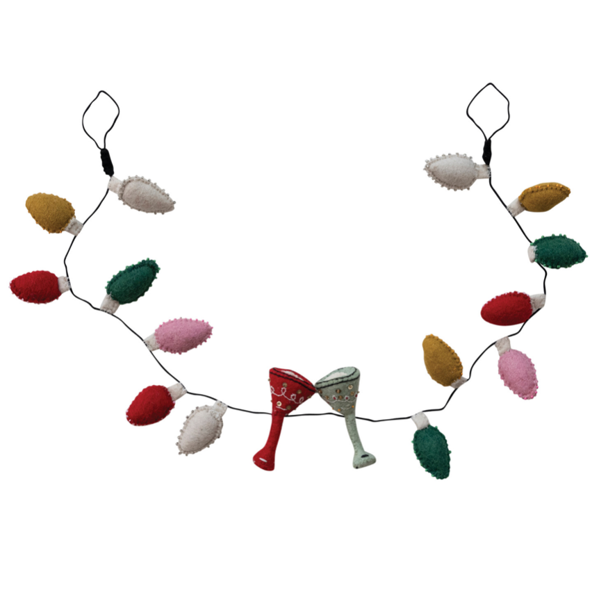 A felt Christmas garland with colorful felt light bulbs and two small felt cocktail glass ornaments hanging from a black string on a plain white 