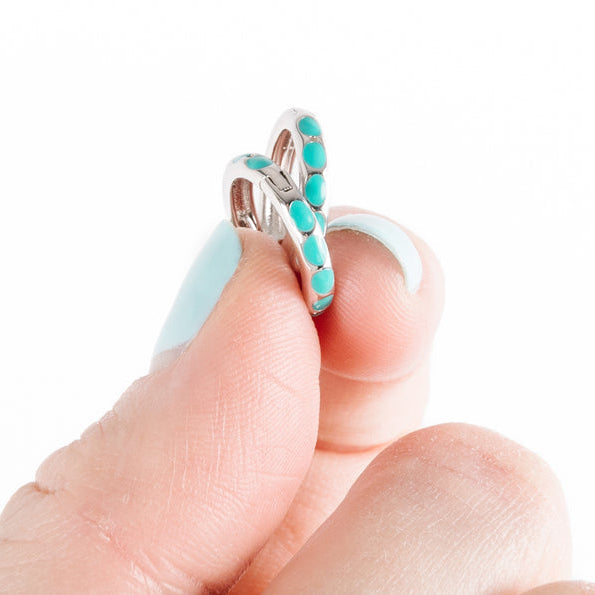 A person's fingertip displaying a silver huggie earring with turquoise accents.