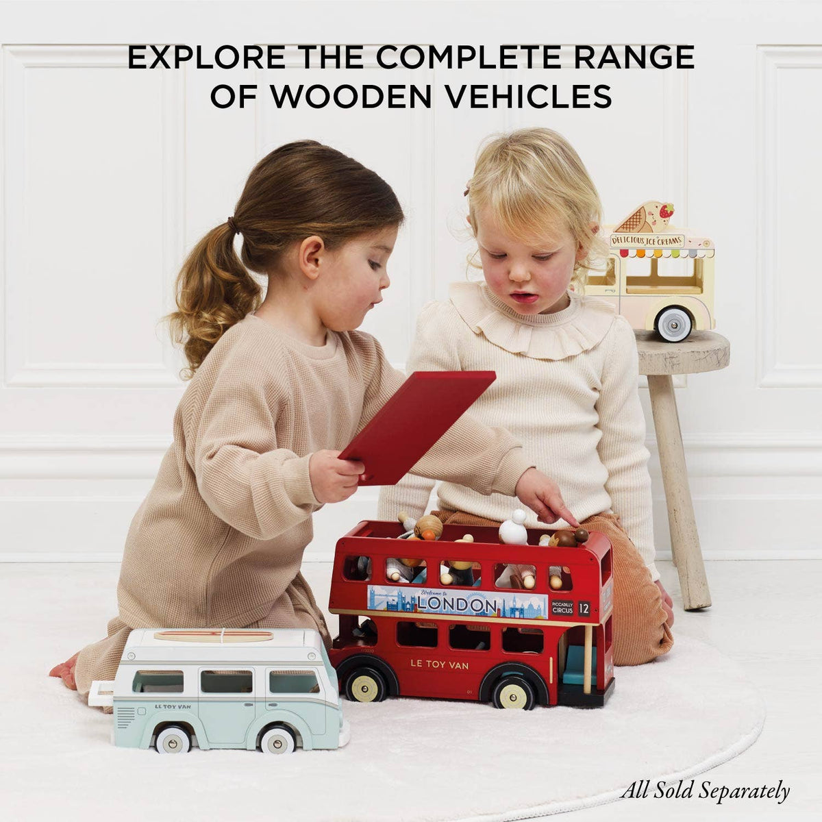 Two children playing with wooden toys including a red London bus and a white van on a light background.