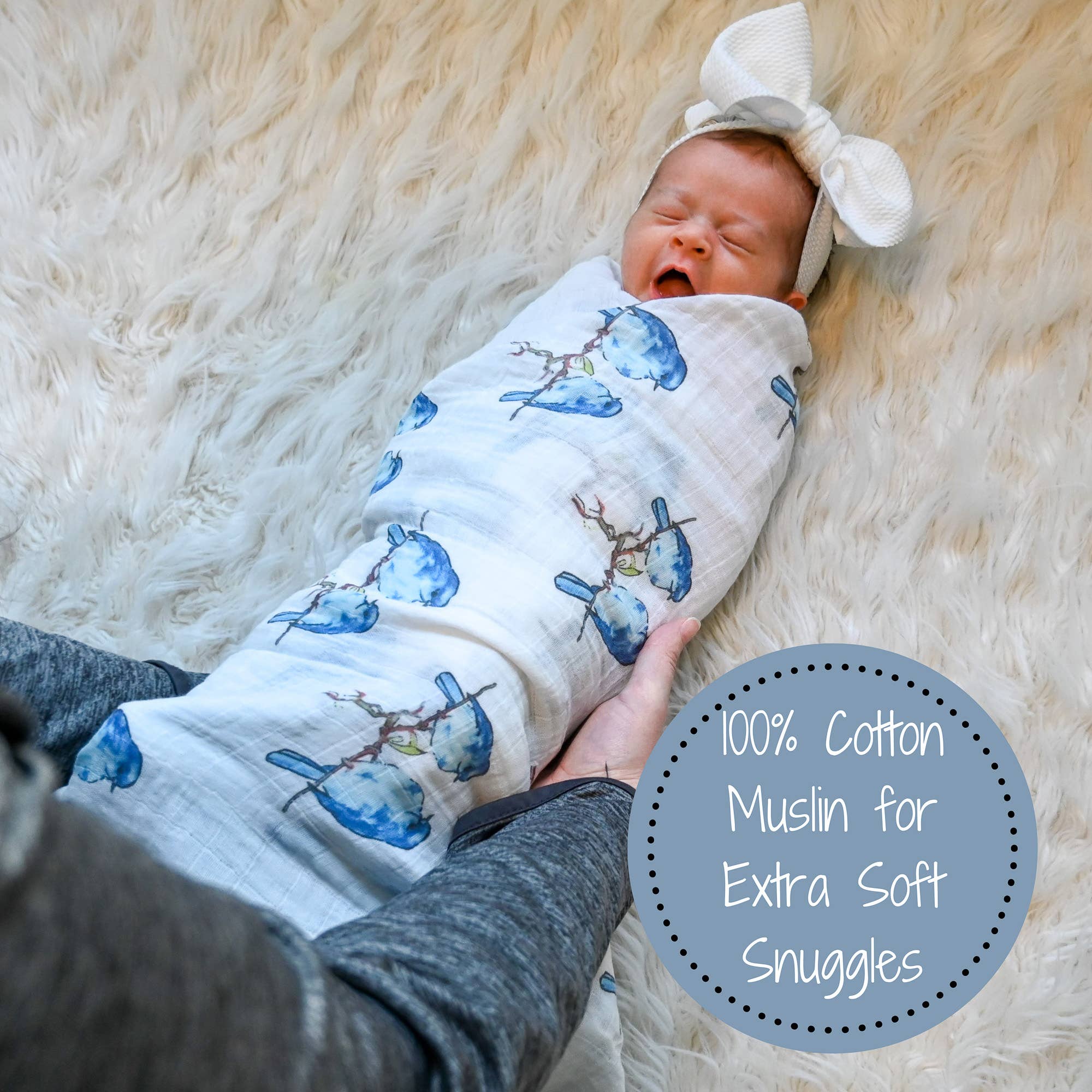 Newborn baby wrapped in a blue and white swaddle with bird patterns on a soft beige surface.