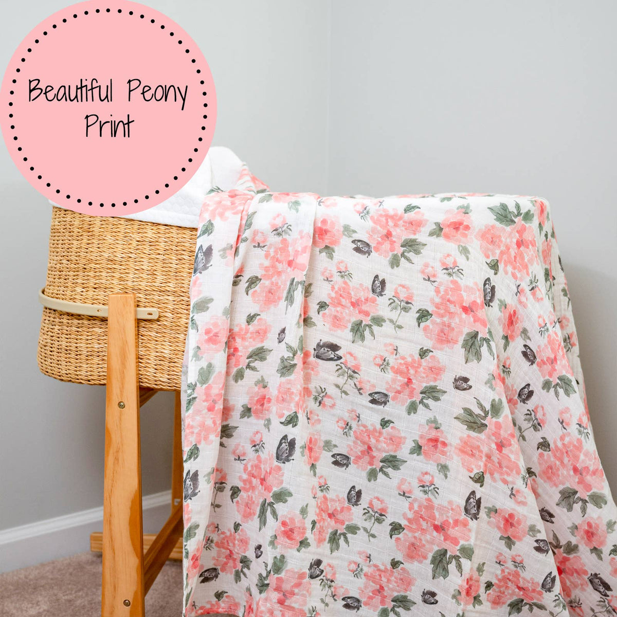 Floral blanket with pink peony pattern draped over a wooden hamper against a gray wall.