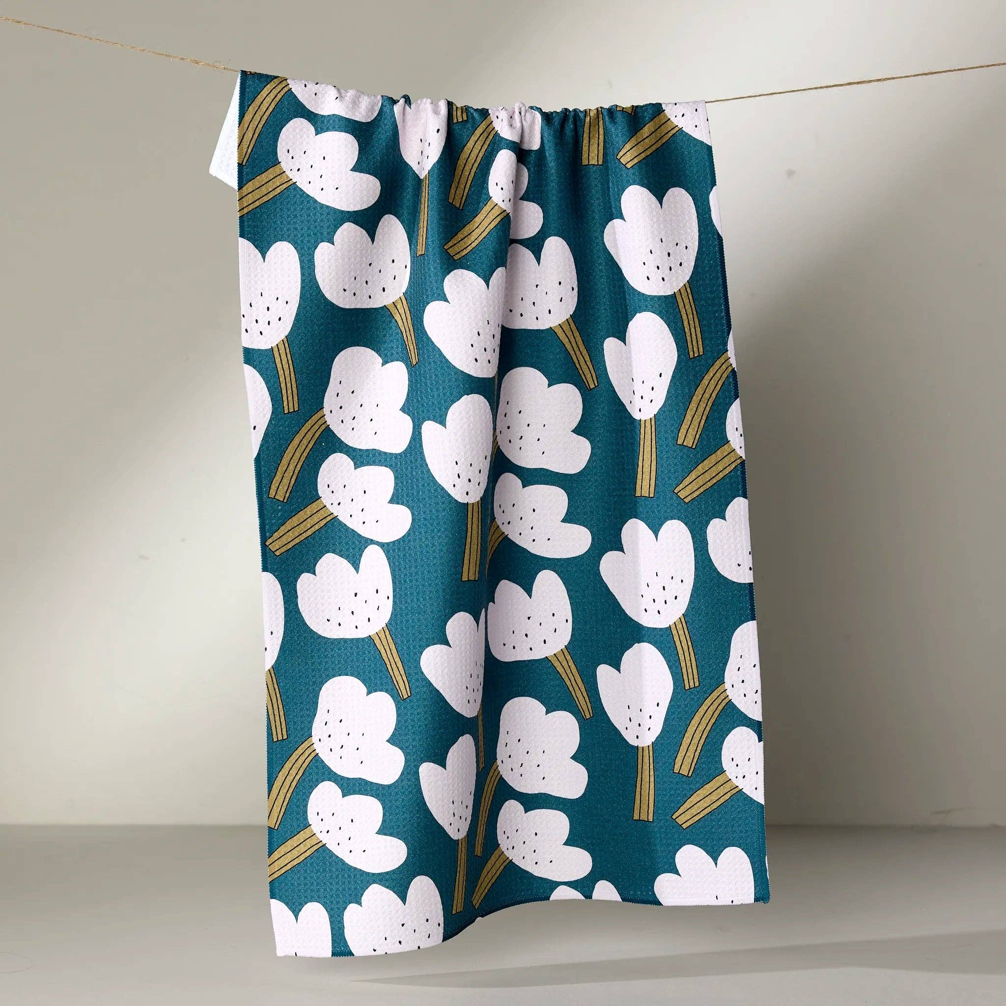 white  tea towel  floral pattern on a teal background hanging against a plain wall.