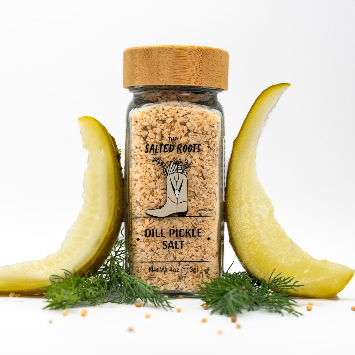 Salt jar with wooden lid and label. Dill pickle spears and dill fronds arranged around jar. 