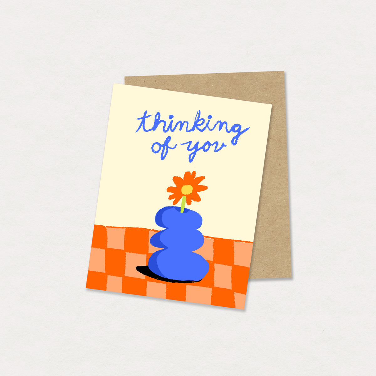 Greeting card with blue object and flower, 'thinking of you' text, on a checkered background.