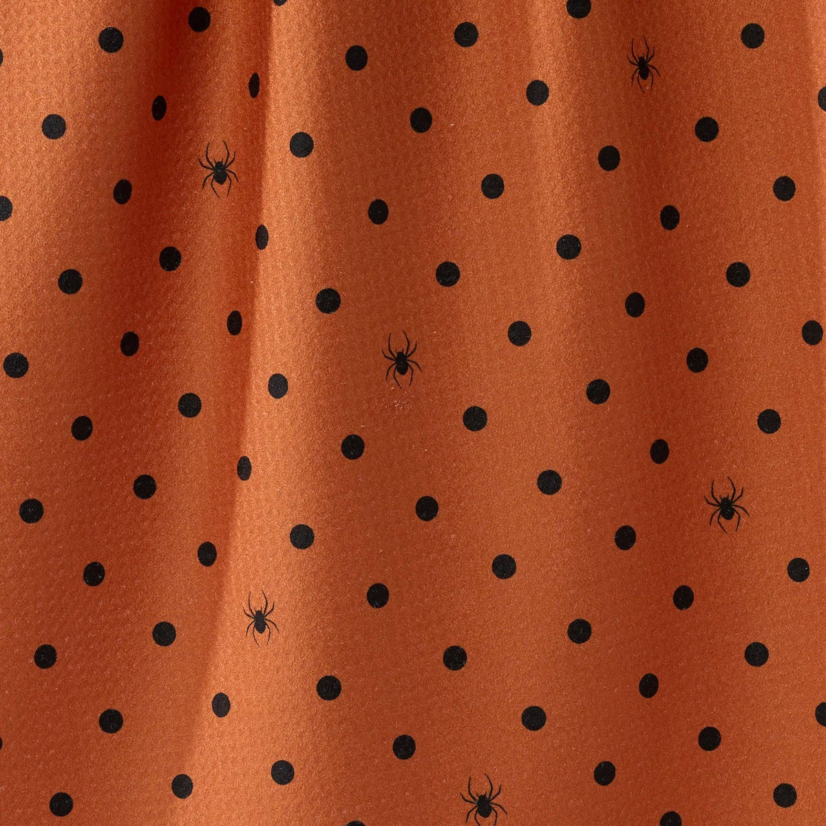 Close-up of an orange tea towel with a black polka dot pattern and small spider motifs.