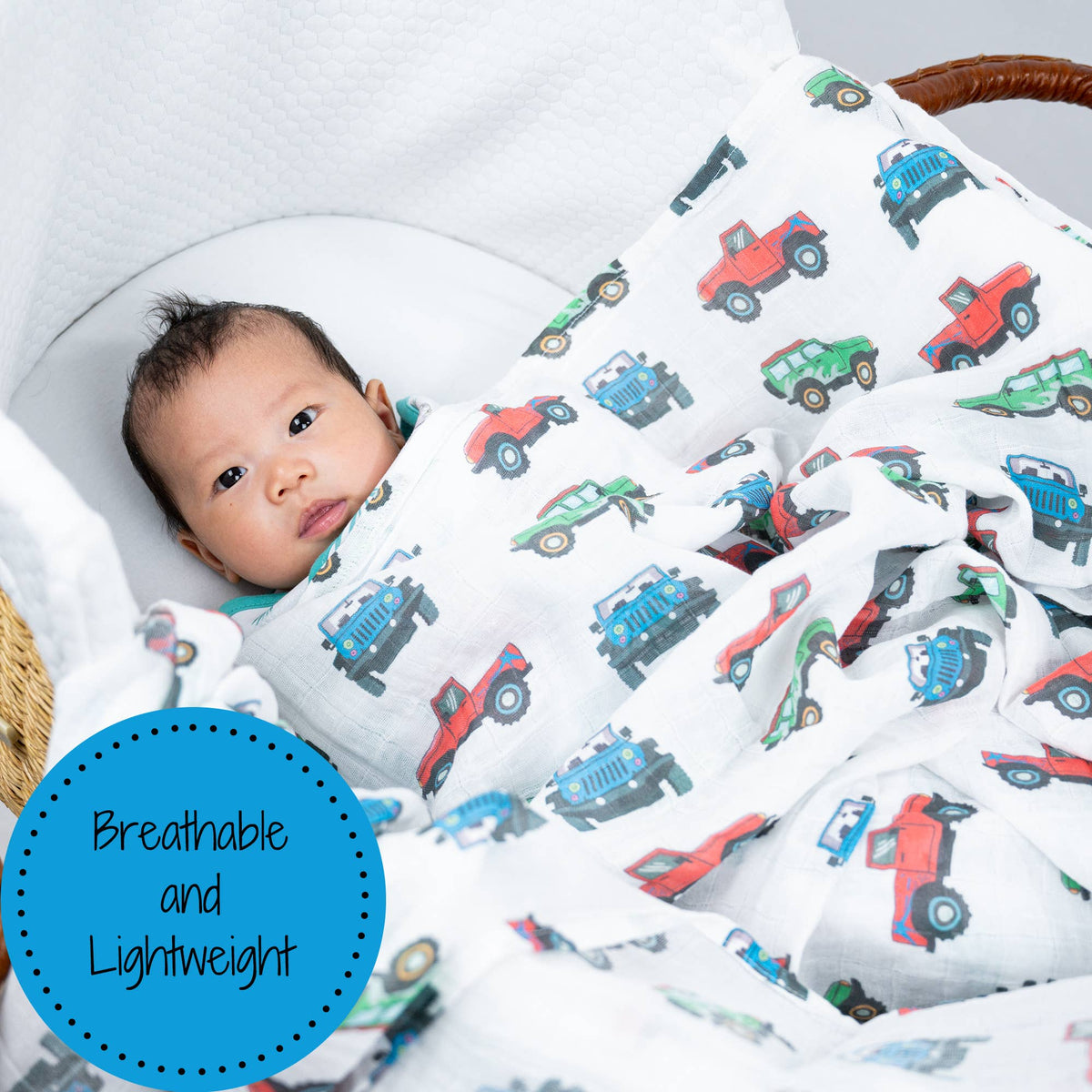 Baby wrapped in a blanket with toy car patterns, lying on a white surface.