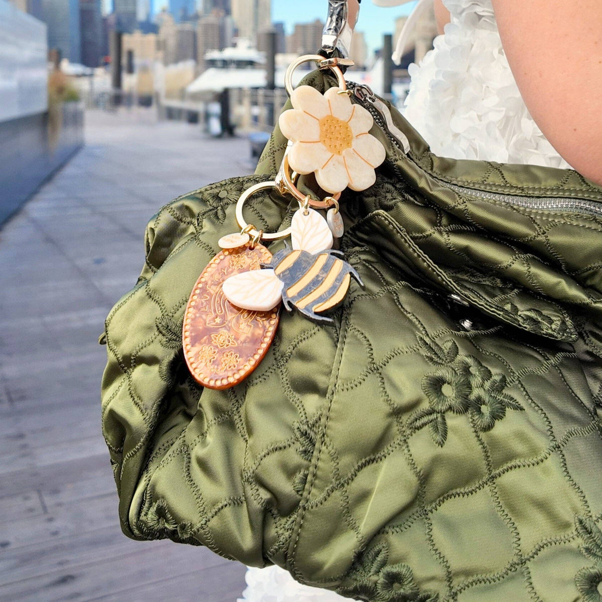 Green quilted bag with decorative keychain against a cityscape background