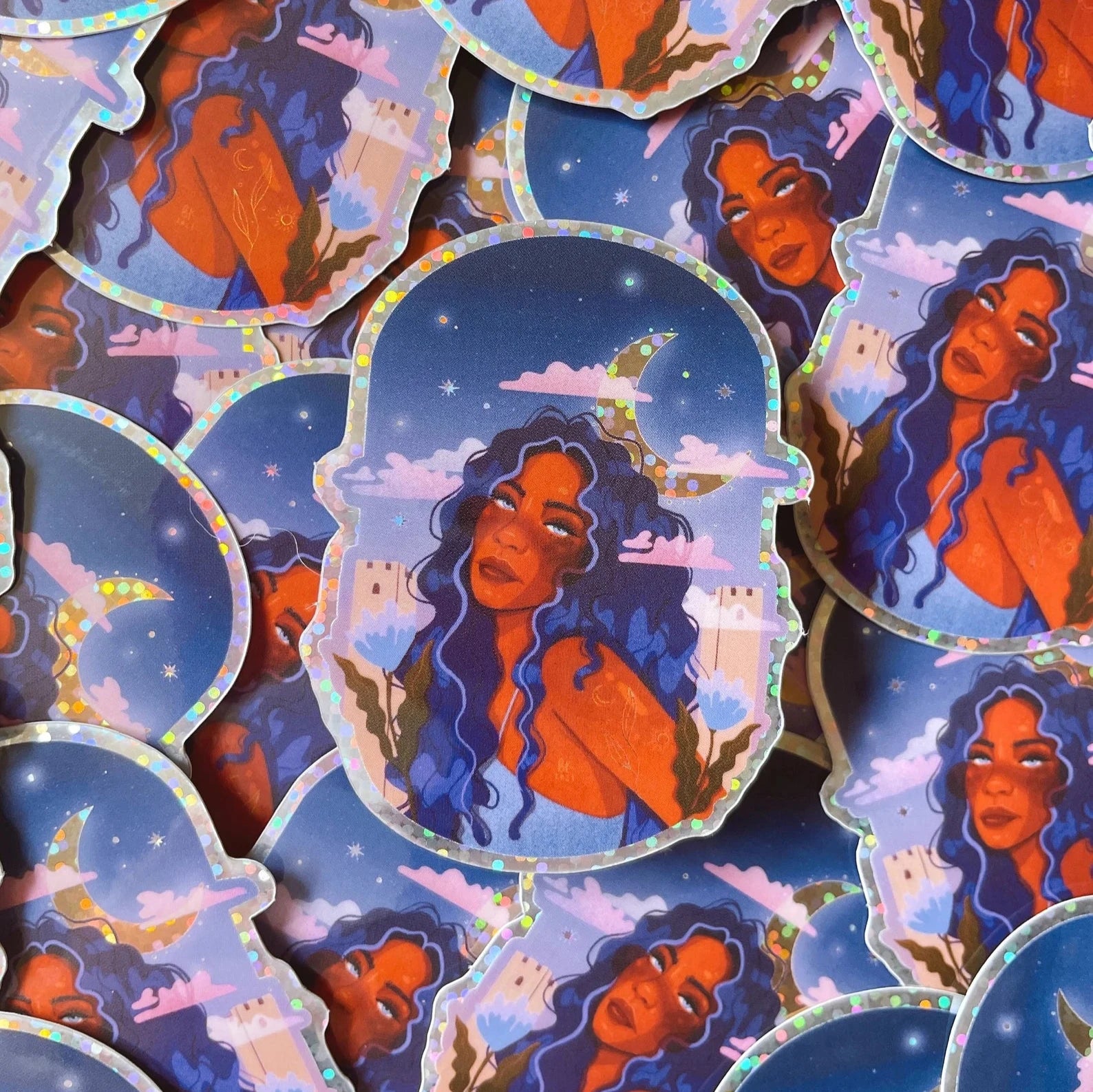 This sticker has a glossy vinyl finish with glitter material. It depicts a black woman with blue-black hair looking into the distance. Behind her is a sparkly crescent moon and the sky has pink and blue hues. 