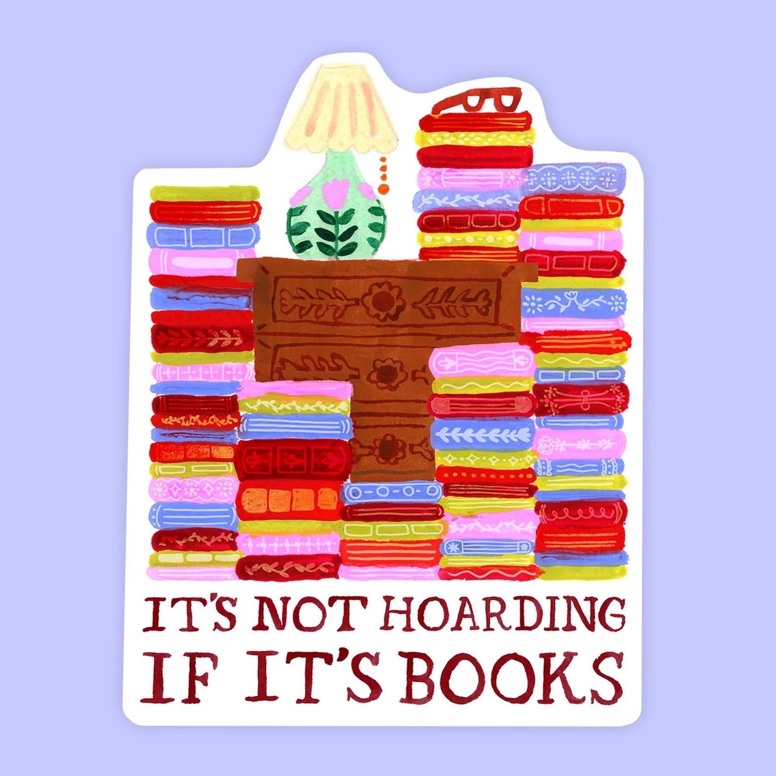 White sticker with stacks of colorful books surrounding a dresser with a cute lamp. Words beneath say "It's not hoarding if its books". 