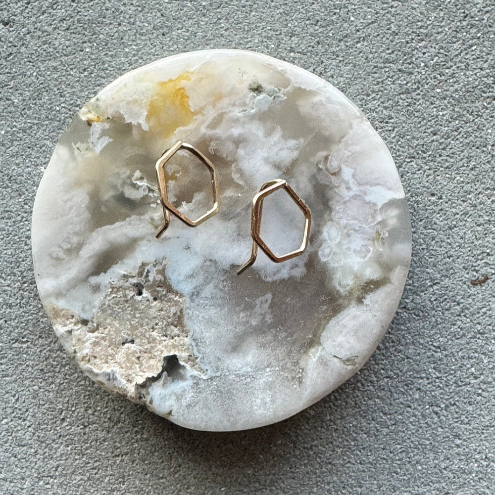 Gold hexagonal earrings on a textured stone surface