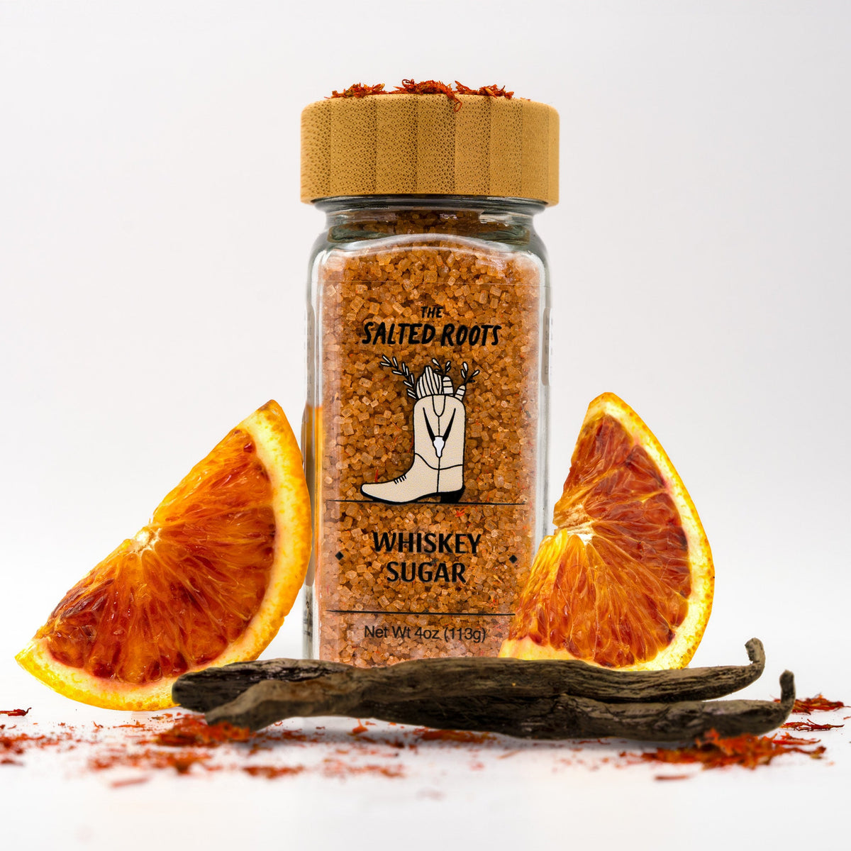 Glass salt jar with wooden lid and labels. Surrounded by orange slices, vanilla bean, and safflower. 
