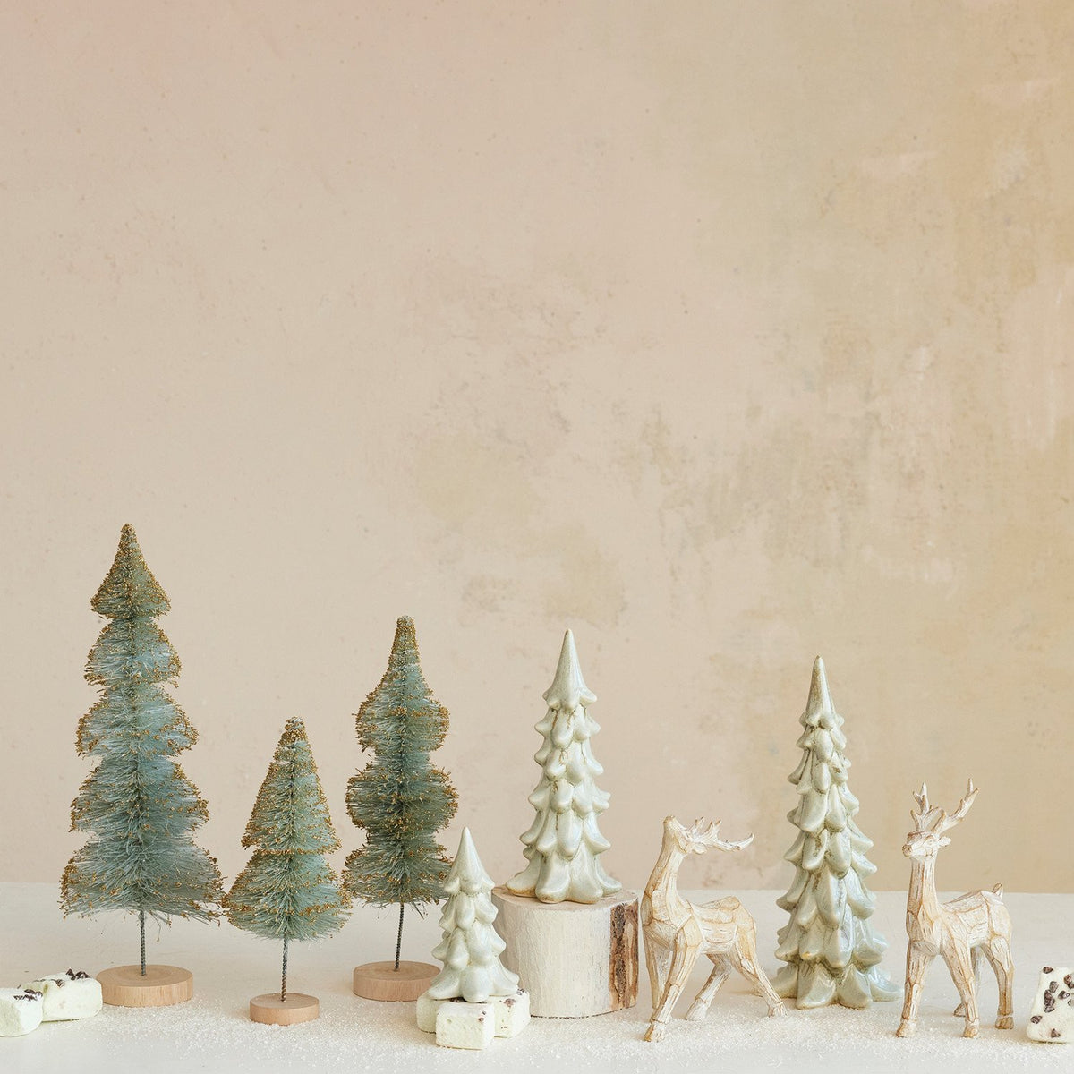 Set of small Christmas trees and deer figurines on a neutral background